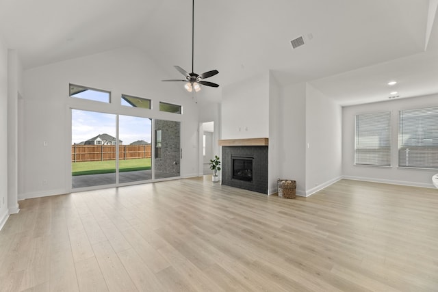 unfurnished living room featuring high vaulted ceiling, ceiling fan, a tile fireplace, and light hardwood / wood-style floors