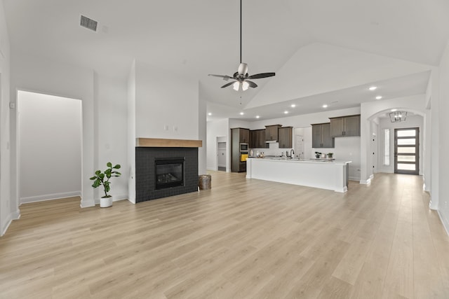 unfurnished living room with sink, a brick fireplace, light hardwood / wood-style flooring, high vaulted ceiling, and ceiling fan with notable chandelier