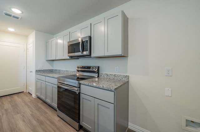 kitchen with appliances with stainless steel finishes, gray cabinetry, light stone counters, and light hardwood / wood-style flooring