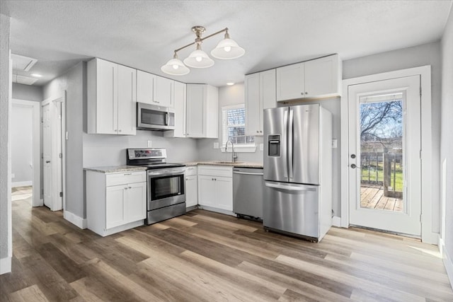 kitchen with pendant lighting, light hardwood / wood-style floors, stainless steel appliances, white cabinets, and light stone counters