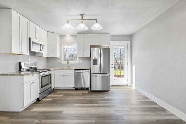 kitchen featuring hanging light fixtures, white cabinetry, appliances with stainless steel finishes, sink, and light hardwood / wood-style flooring