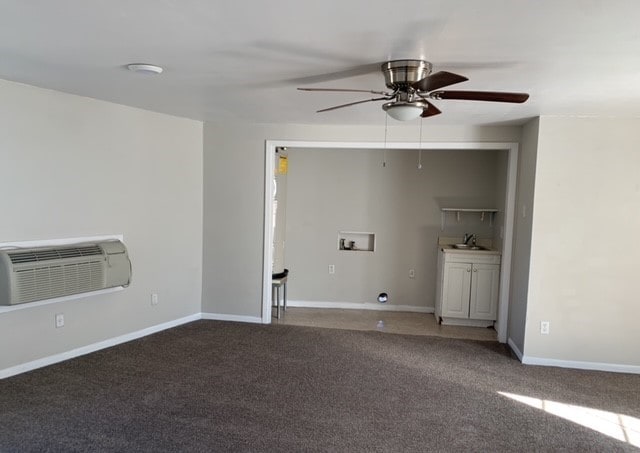 spare room with ceiling fan, sink, dark colored carpet, and a wall mounted air conditioner