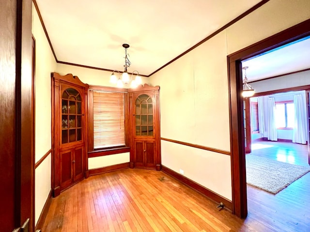 unfurnished room featuring light hardwood / wood-style flooring, crown molding, and a notable chandelier