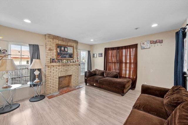 living room with brick wall, light wood-type flooring, and a brick fireplace