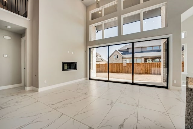 unfurnished room featuring marble finish floor, a towering ceiling, and baseboards