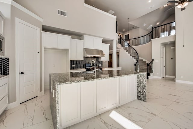 kitchen featuring visible vents, dark stone counters, an island with sink, marble finish floor, and under cabinet range hood