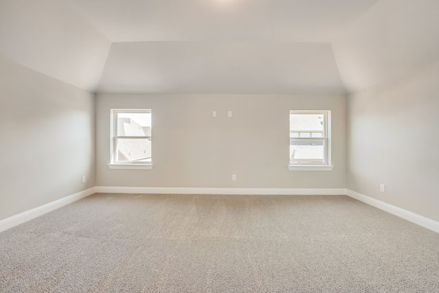 spare room featuring light colored carpet, vaulted ceiling, and baseboards