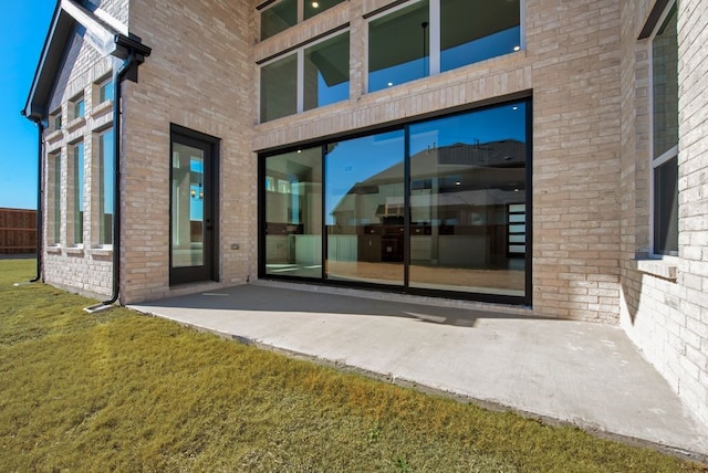 entrance to property featuring brick siding, a lawn, and a patio area