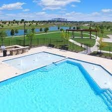 outdoor pool with a patio area, fence, a lawn, and a water view