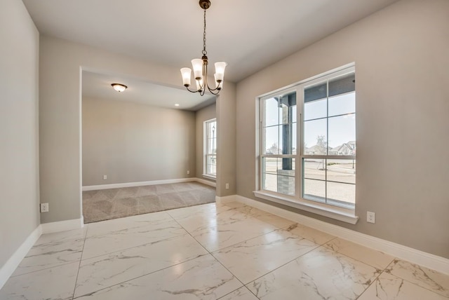 empty room featuring marble finish floor, an inviting chandelier, and baseboards