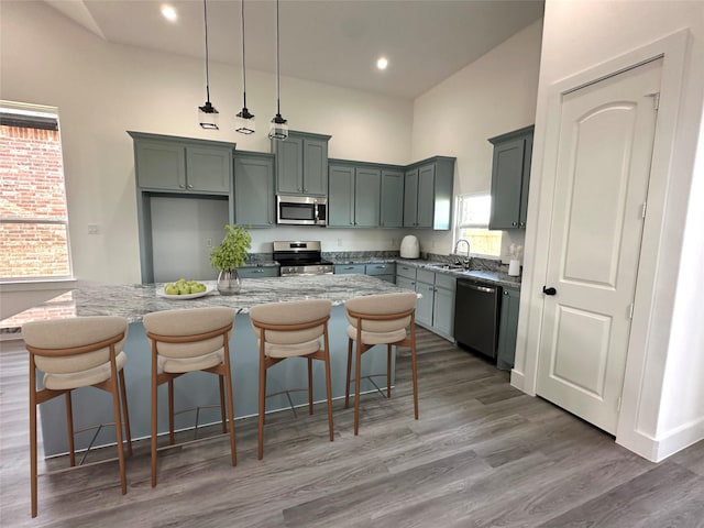 kitchen with light stone countertops, a center island, hanging light fixtures, stainless steel appliances, and sink