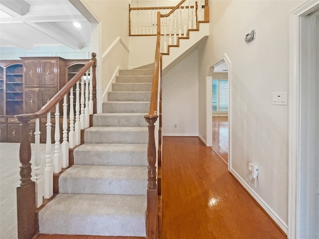 stairway featuring coffered ceiling, beam ceiling, and hardwood / wood-style flooring