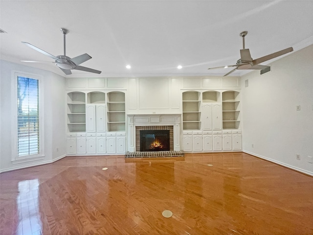 unfurnished living room featuring ceiling fan, a fireplace, built in shelves, and hardwood / wood-style flooring