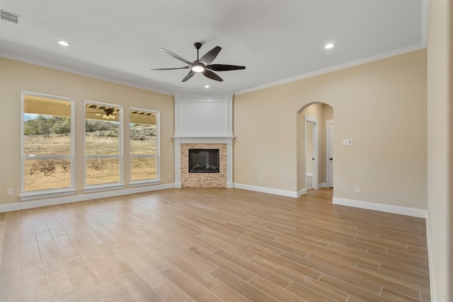 unfurnished living room featuring ceiling fan, crown molding, light hardwood / wood-style floors, and a stone fireplace