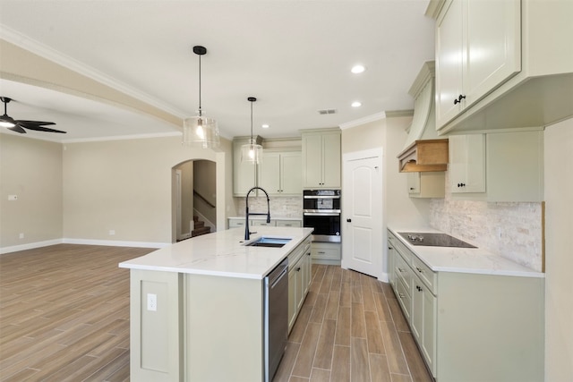 kitchen with an island with sink, ceiling fan, backsplash, stainless steel appliances, and decorative light fixtures