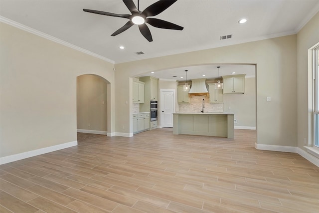 unfurnished living room featuring ceiling fan, crown molding, sink, and plenty of natural light