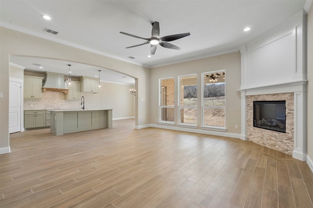 unfurnished living room with ornamental molding, sink, ceiling fan, and light wood-type flooring