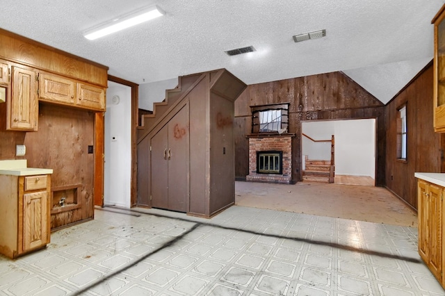 kitchen with wood walls, lofted ceiling, a textured ceiling, and a brick fireplace