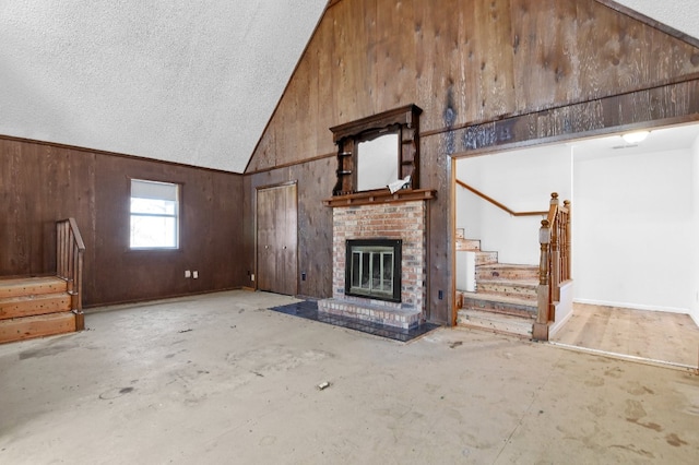 unfurnished living room with high vaulted ceiling, a brick fireplace, a textured ceiling, and wood walls