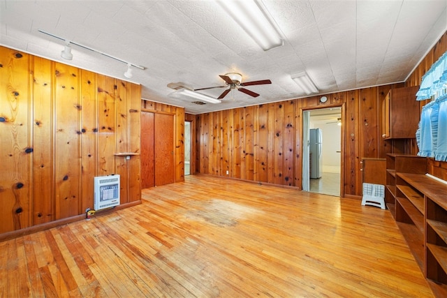 empty room featuring wooden walls, ceiling fan, track lighting, and light hardwood / wood-style flooring