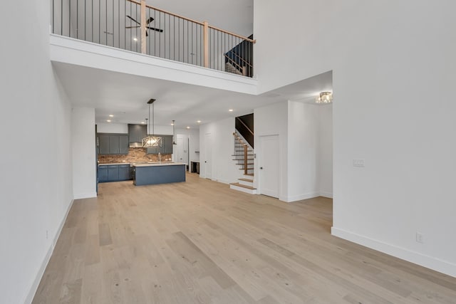 unfurnished living room with light hardwood / wood-style floors, sink, ceiling fan, and a towering ceiling