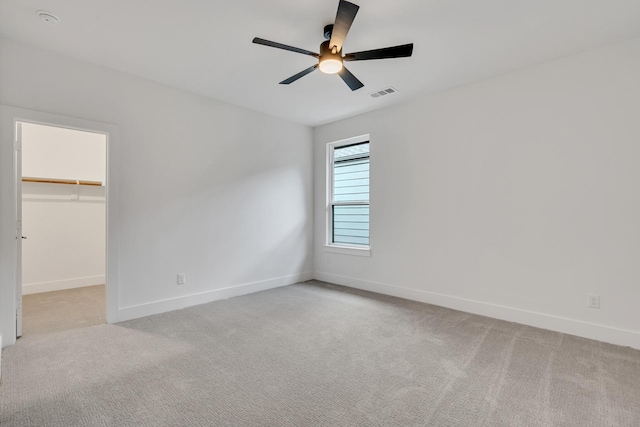 unfurnished bedroom with ceiling fan, light carpet, a closet, and a walk in closet