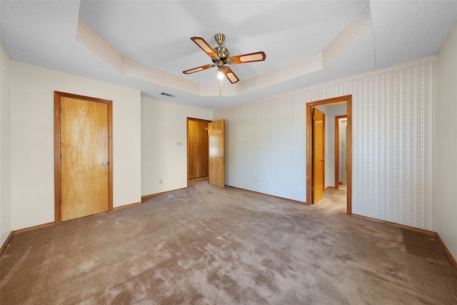 unfurnished bedroom featuring ceiling fan, a tray ceiling, a textured ceiling, and carpet flooring