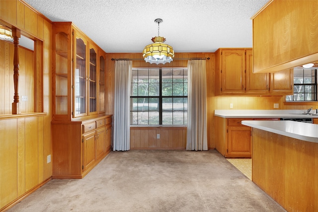 kitchen with light colored carpet, decorative light fixtures, sink, wooden walls, and a textured ceiling