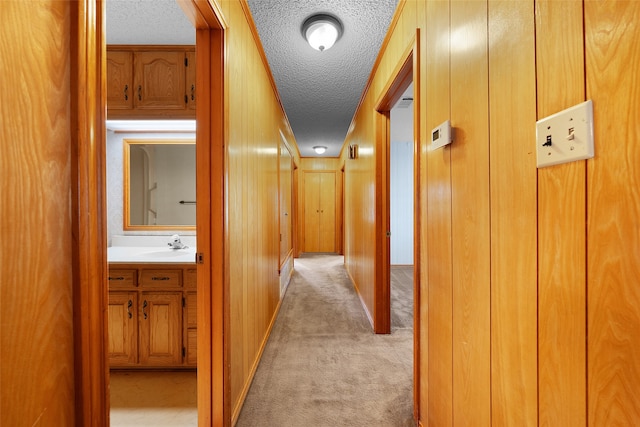 hallway featuring light colored carpet, sink, wooden walls, and a textured ceiling