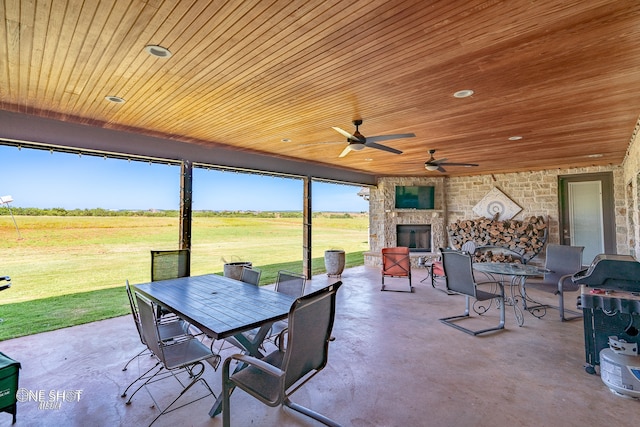 view of patio with an outdoor stone fireplace, a rural view, and ceiling fan