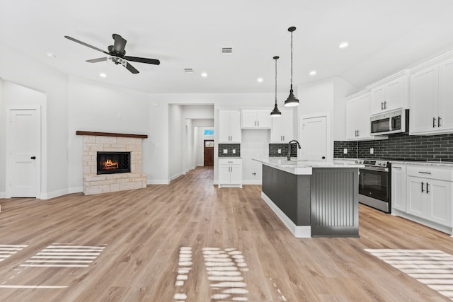 kitchen with pendant lighting, a kitchen island with sink, light hardwood / wood-style flooring, white cabinetry, and stainless steel appliances