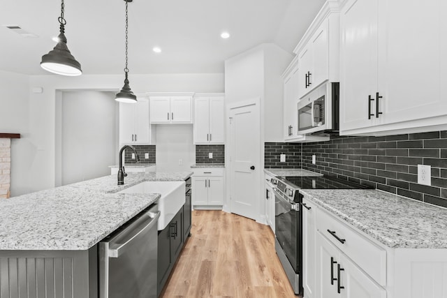 kitchen with white cabinets, hanging light fixtures, light wood-type flooring, an island with sink, and appliances with stainless steel finishes