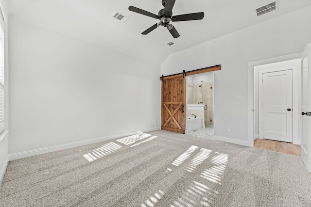 unfurnished bedroom with connected bathroom, ceiling fan, a barn door, light colored carpet, and lofted ceiling