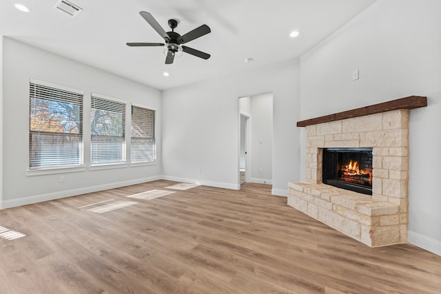 unfurnished living room featuring a stone fireplace, ceiling fan, and light hardwood / wood-style flooring