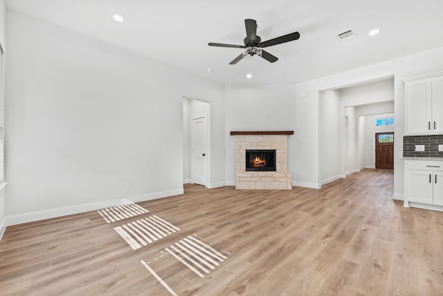 unfurnished living room with light wood-type flooring, a stone fireplace, and ceiling fan