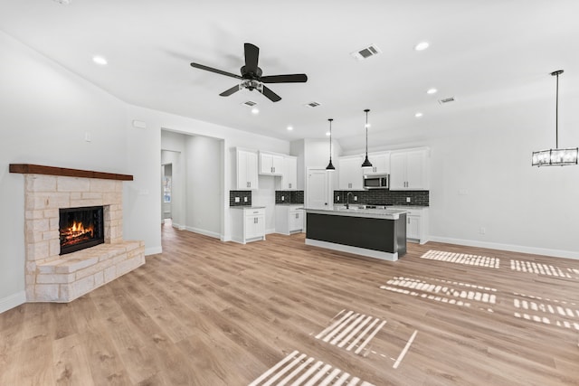 unfurnished living room with a fireplace, ceiling fan, light hardwood / wood-style flooring, and sink