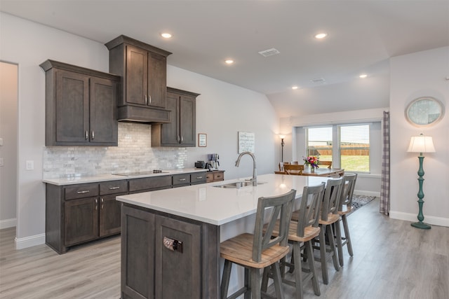 kitchen featuring a kitchen island with sink, sink, light wood-type flooring, a kitchen bar, and dark brown cabinetry