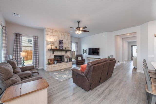 living area with a fireplace, a ceiling fan, baseboards, visible vents, and light wood-style floors