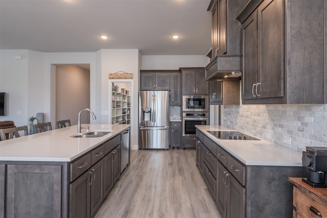 kitchen with sink, light hardwood / wood-style floors, a breakfast bar area, a kitchen island with sink, and appliances with stainless steel finishes