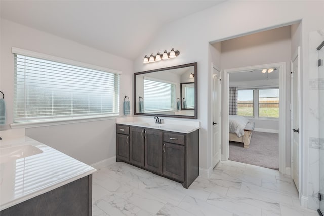 ensuite bathroom featuring vaulted ceiling, marble finish floor, a sink, and two vanities