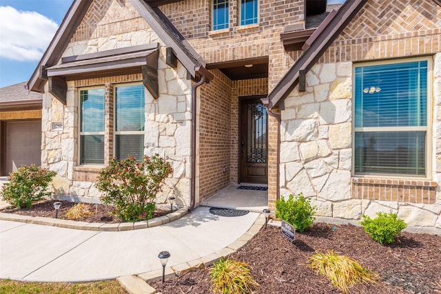 entrance to property with a garage, stone siding, and brick siding