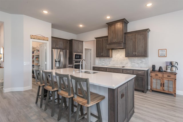 kitchen with dark brown cabinetry, stainless steel appliances, a sink, a kitchen breakfast bar, and a center island with sink