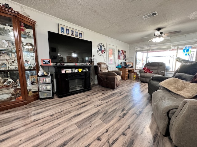 living room with a textured ceiling, ceiling fan, light wood-type flooring, and crown molding