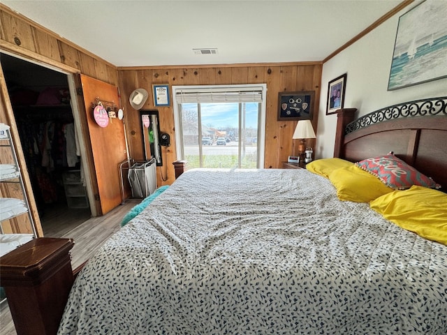 bedroom featuring a closet, wooden walls, crown molding, and light hardwood / wood-style floors