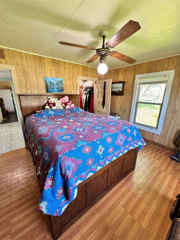 bedroom with light wood-type flooring, ceiling fan, a closet, wood walls, and a textured ceiling