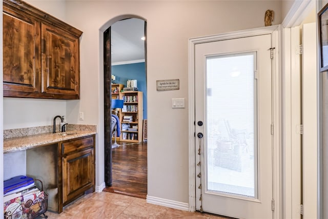 doorway with crown molding, sink, and light tile floors