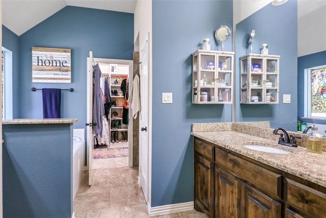 bathroom featuring tile flooring, vaulted ceiling, oversized vanity, and a tub