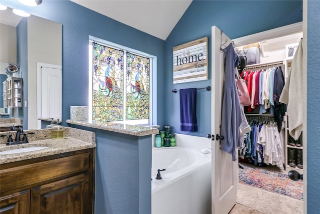 bathroom with large vanity, vaulted ceiling, and a bathtub