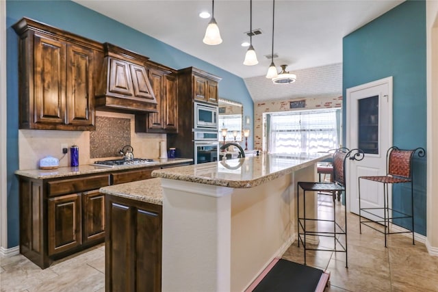 kitchen featuring an island with sink, decorative light fixtures, custom exhaust hood, appliances with stainless steel finishes, and backsplash