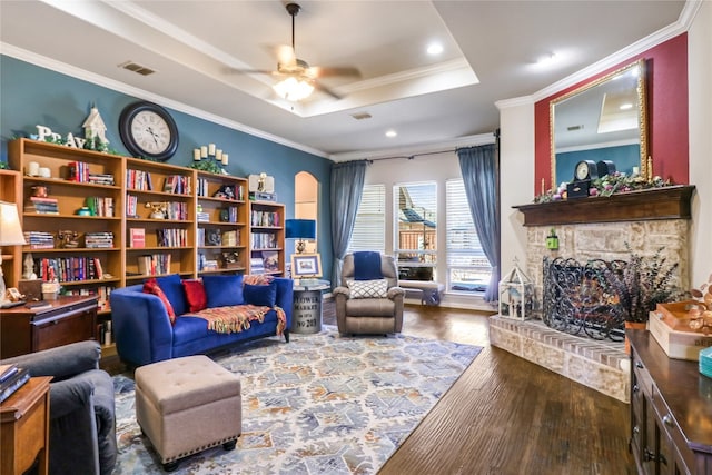 living room with dark hardwood / wood-style floors, a tray ceiling, ceiling fan, a fireplace, and ornamental molding